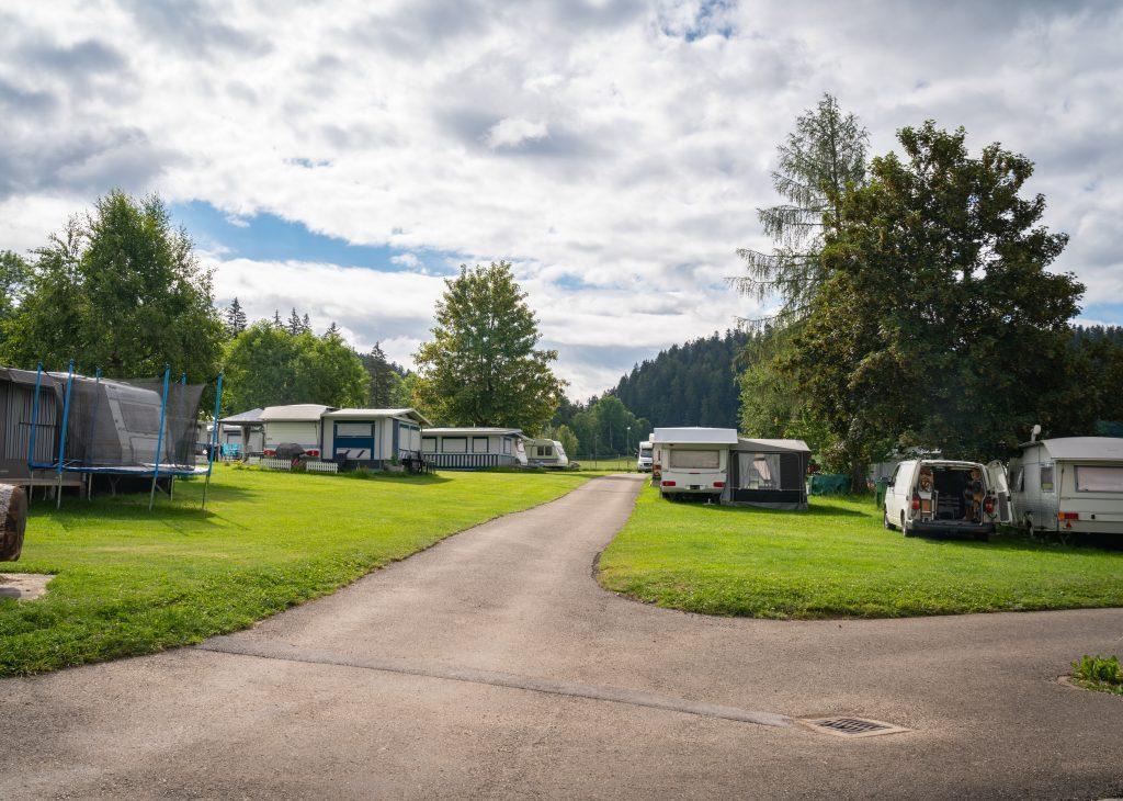 Wiesen-Stellplätze mit Campers und Trampolin, Wald im Hintergrund - Camping Jura