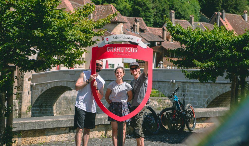 zwei junge Männer und eine Frau hinter dem Grand Tour Fotorahmen in Saint-Ursanne