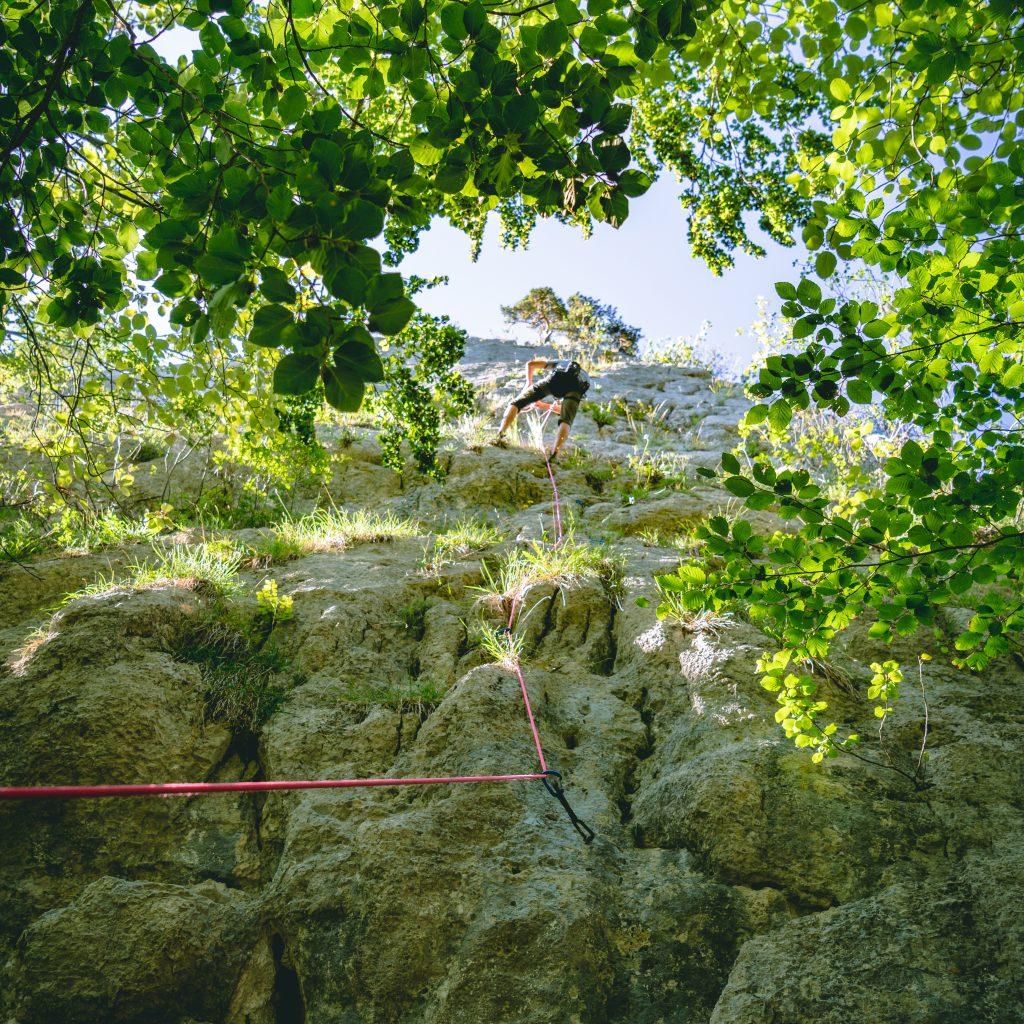 Gesicherter Kletterer an der Felswand - Bodenperspektive - Ferien im Jura