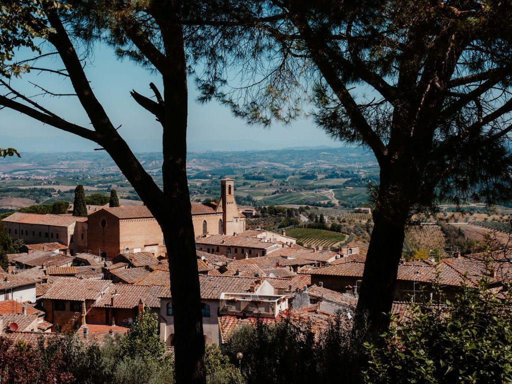 Rundreise Toskana, Blick zwischen Bäumen auf rote Gebäude von Siena