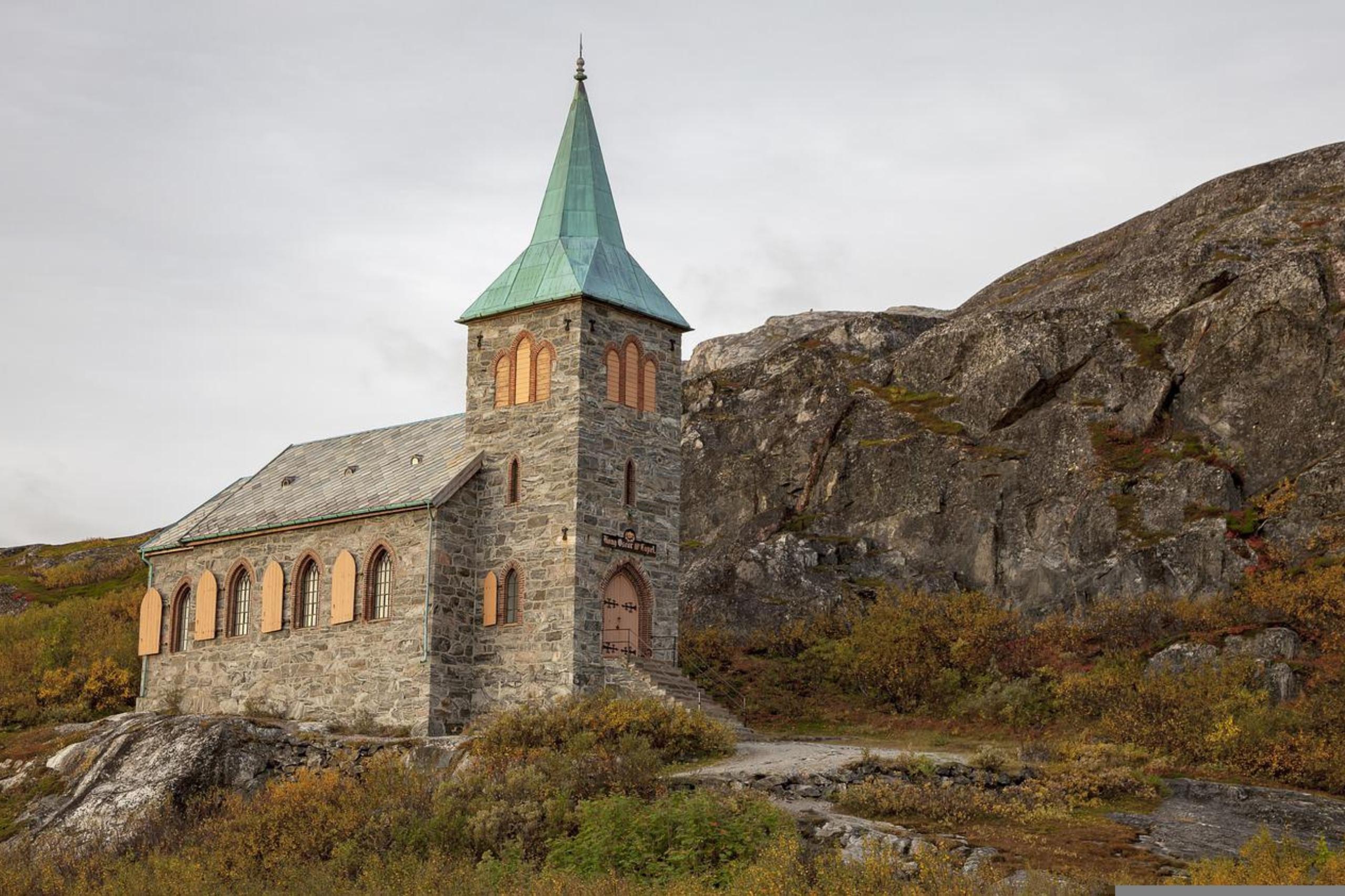 Eine kleine Steinkirche mit Bergen im Hintergrund.