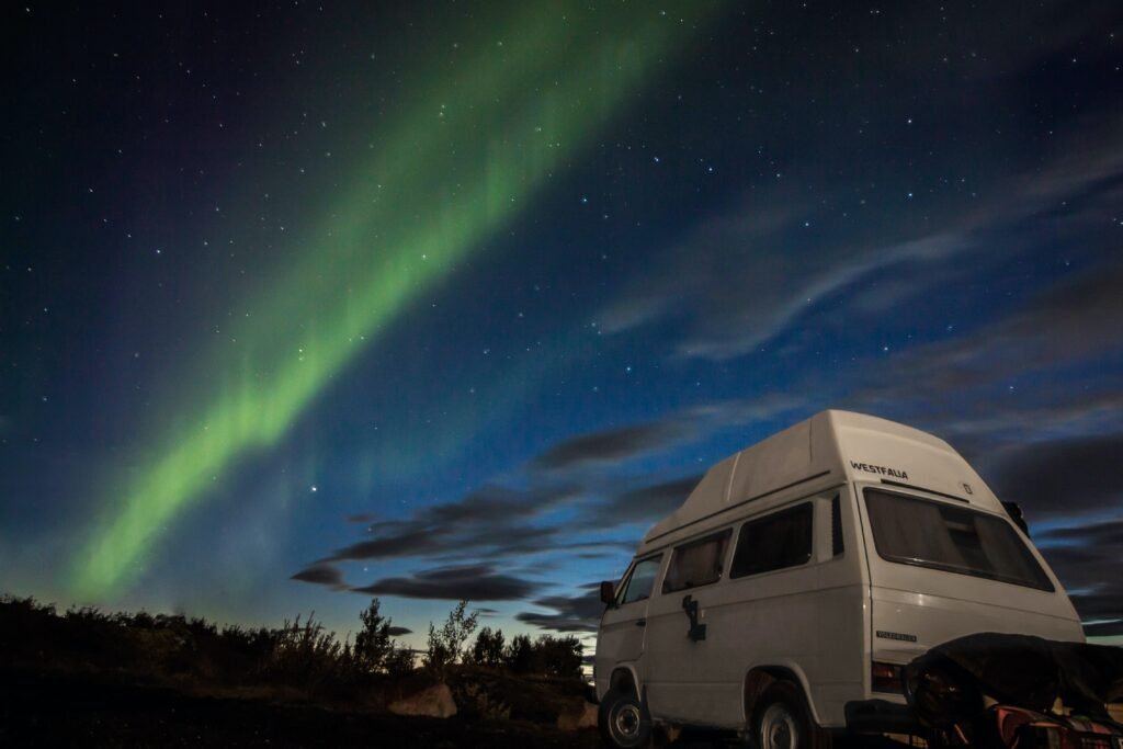 Un camping-car garé en pleine nature avec une aurore boréale en arrière-plan.